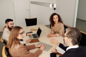Fem personer diskuterar vid ett konferensbord med laptop och anteckningar