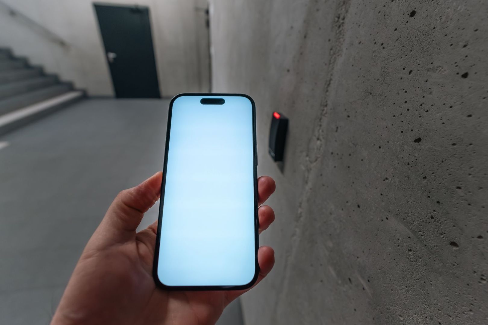 Hand håller en smartphone nära en väggmonterad kortläsare med röd lampa